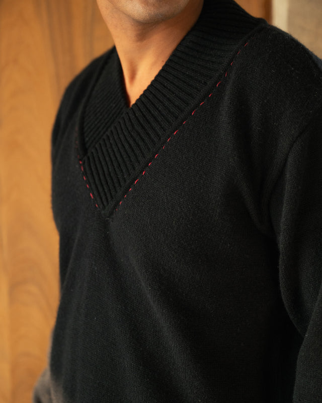 Black sweater with red stitching detail on a wooden background