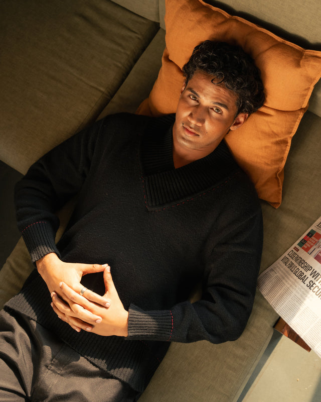 Man lying on a couch with a newspaper, surrounded by pillows