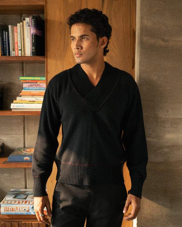 Man wearing a black sweater standing in a room with wooden shelves and books.