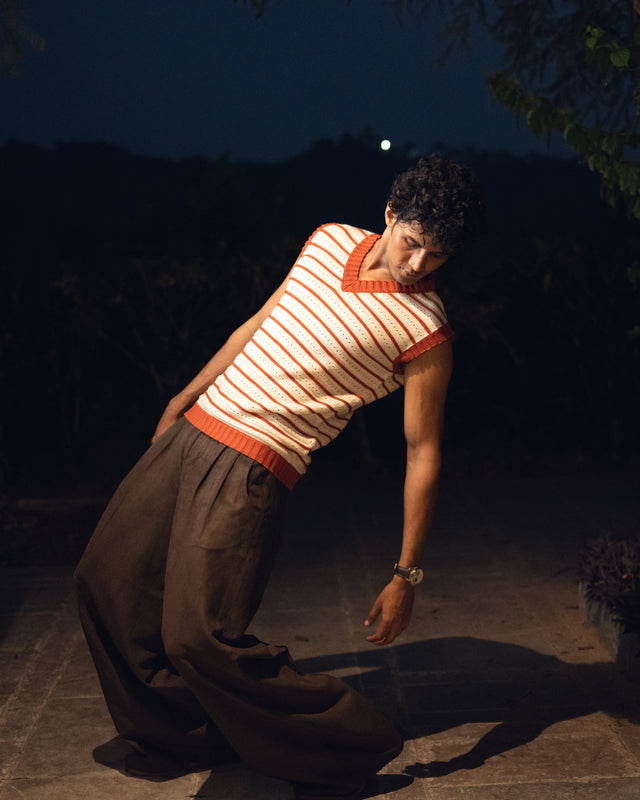 Person in striped shirt and wide-leg pants crouching outdoors at night.